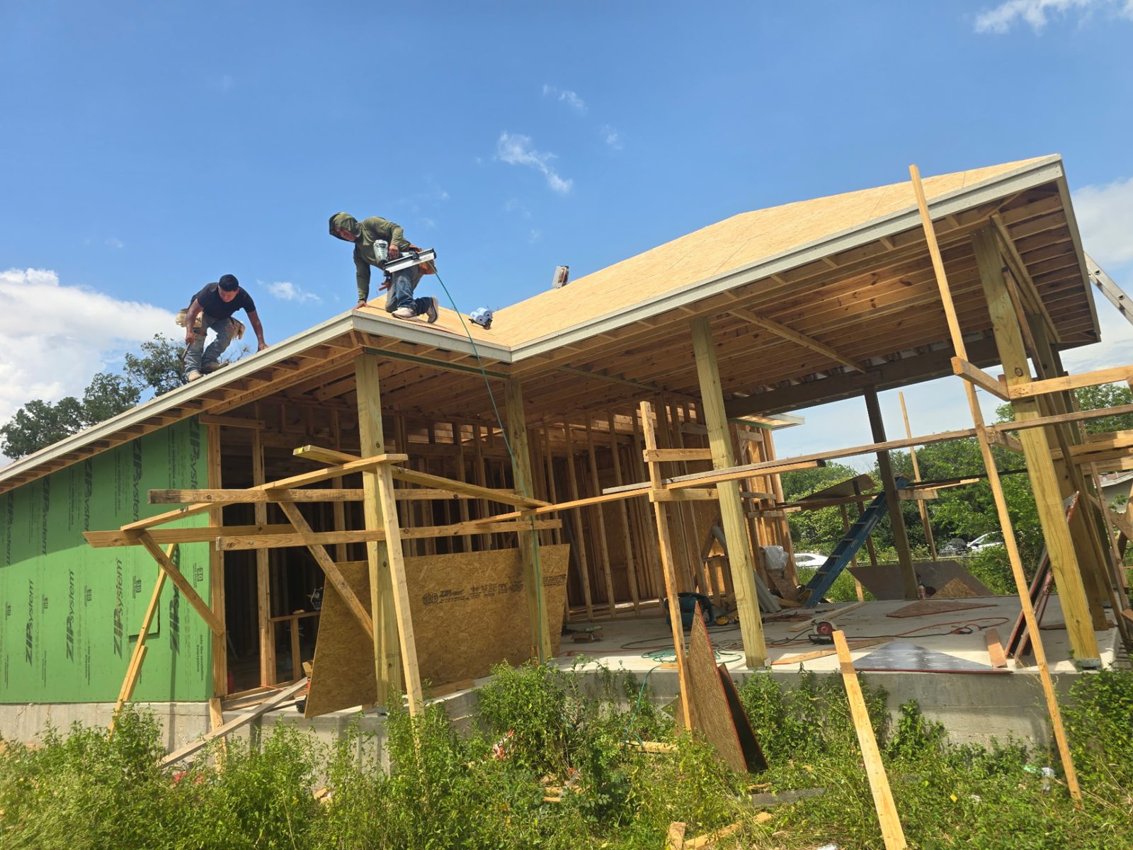 Two crew members nailing plywood roof decking on a new house frame