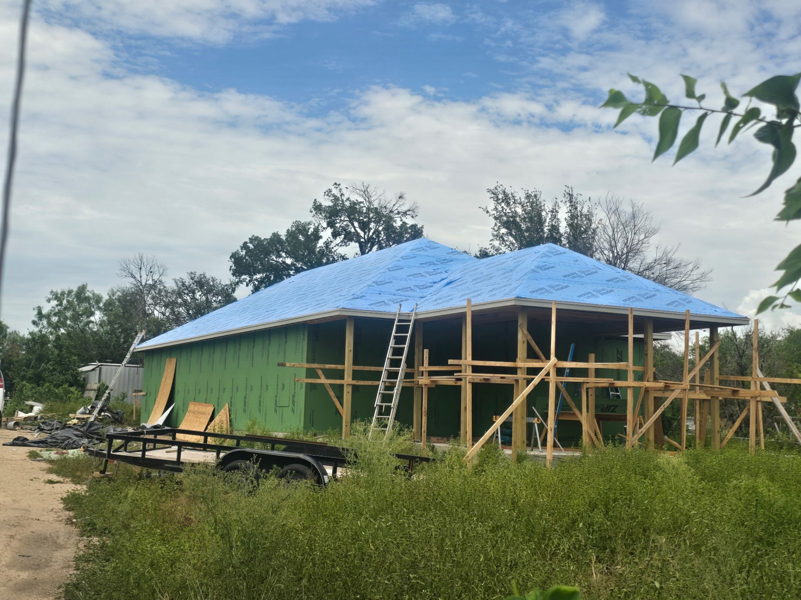 Hip roof covered with blue synthetic underlayment over green sheathing